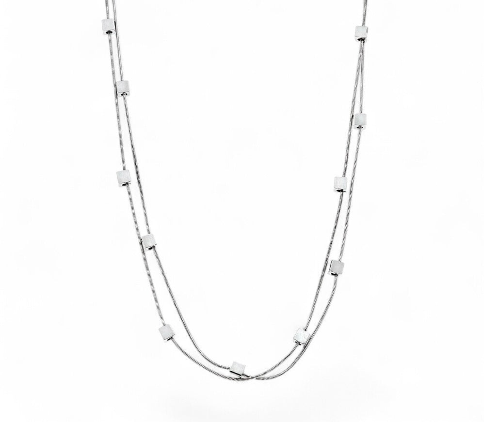 A striking double snake chain necklace featuring expressive square cube accents. Available in silver and gold. 

Een opvallende dubbele slangenketting met expressieve vierkante kubusaccenten. Verkrijgbaar in zilver en goud.

Un superbe collier à double chaîne serpent avec des accents de cubes carrés expressifs. Disponible en argent et or.